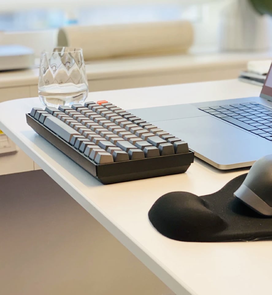 glass and keyboard near a laptop on a desk